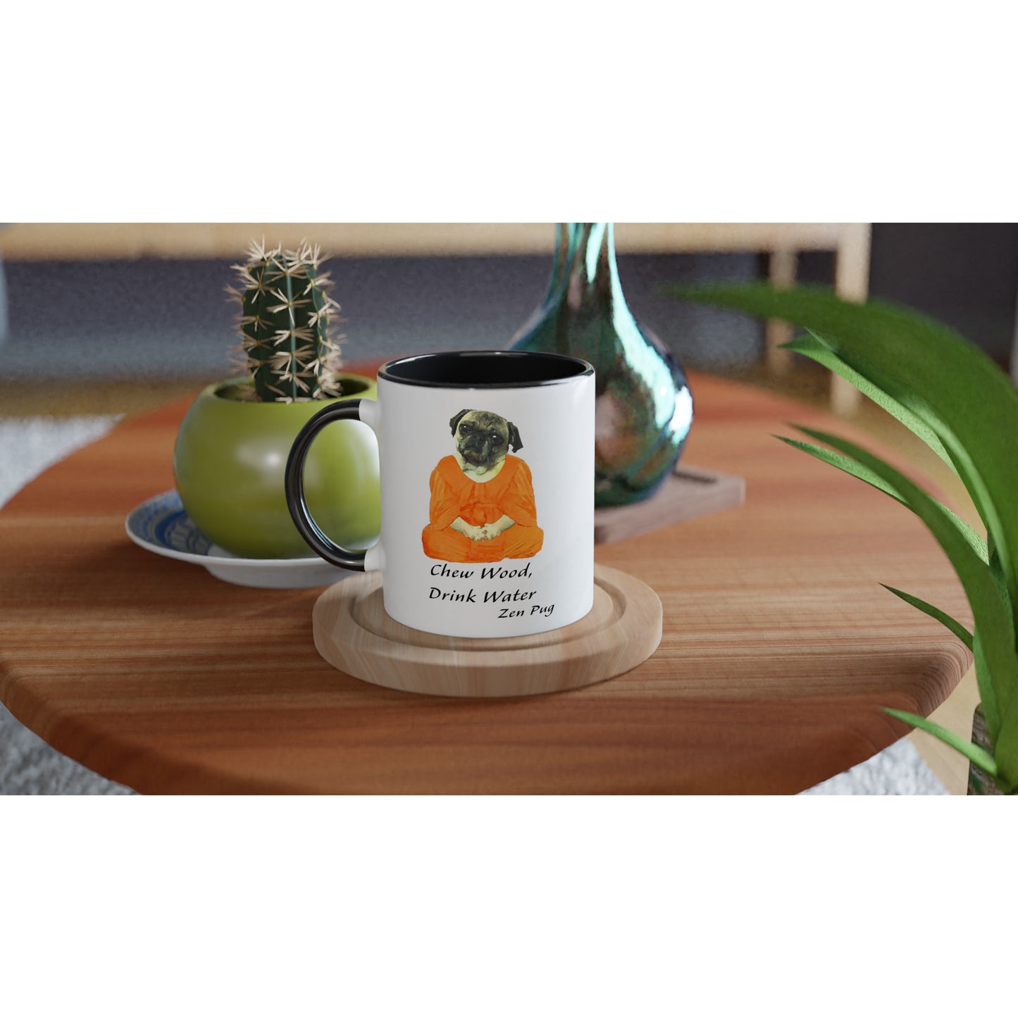 Round wooden end table with a potted cactus, glass vase, and white mug on it. The mug has a black handle, rim, and inside and has a picture of a pug sitting cross-legged in an orange monk robe. Below the image are then words " Chew wood, drink water. Zen pug"