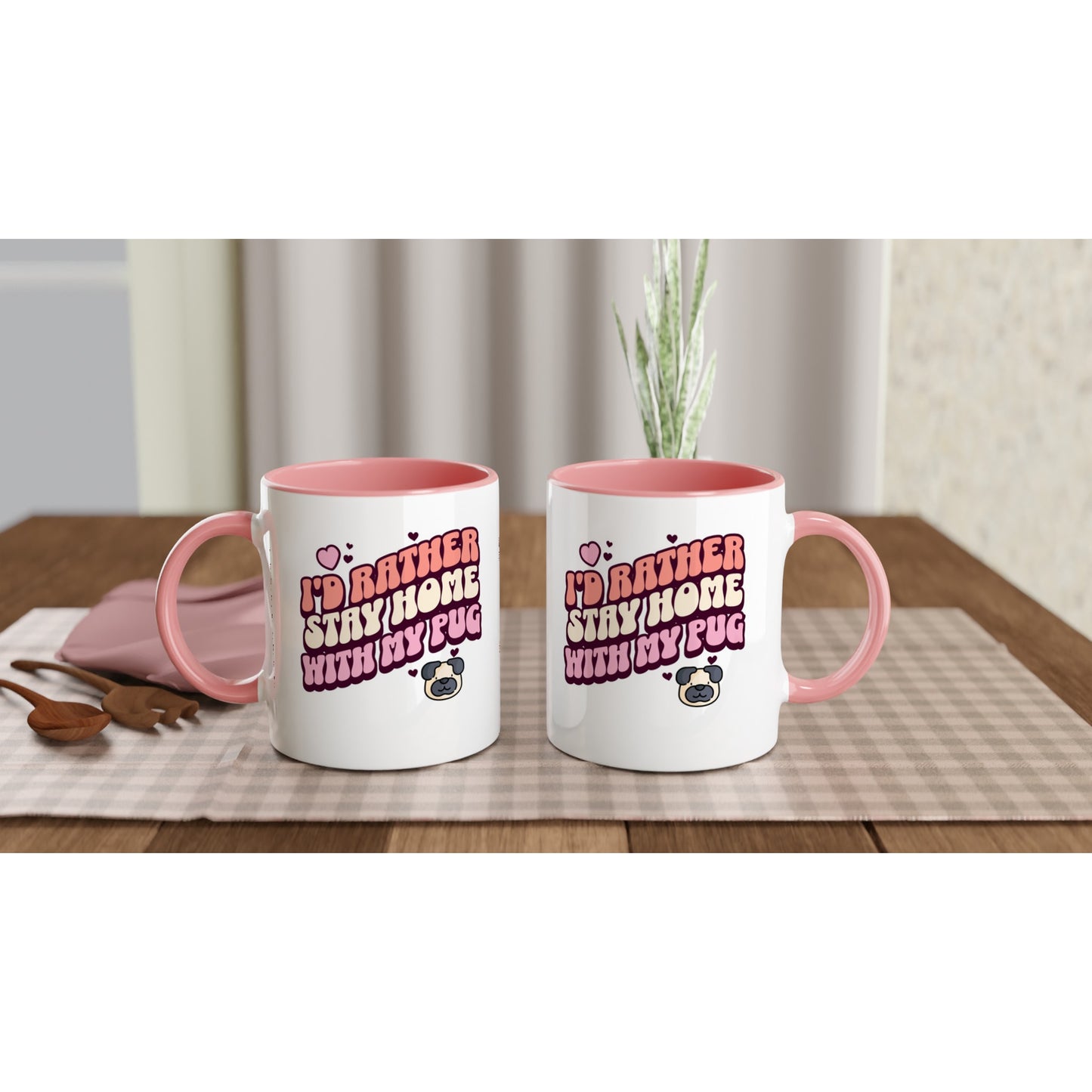 Two white mugs with pink handles and pink insides showing off the front and back of the mug with the words "I'd rather stay home with my pug" in an orangey-pink, beige, and pink colored bubble-style lettering on it and small hearts above the words to the left and a small heart above the words to the right with two other small hearts and a picture of a cartoon pug face below the words on the right.