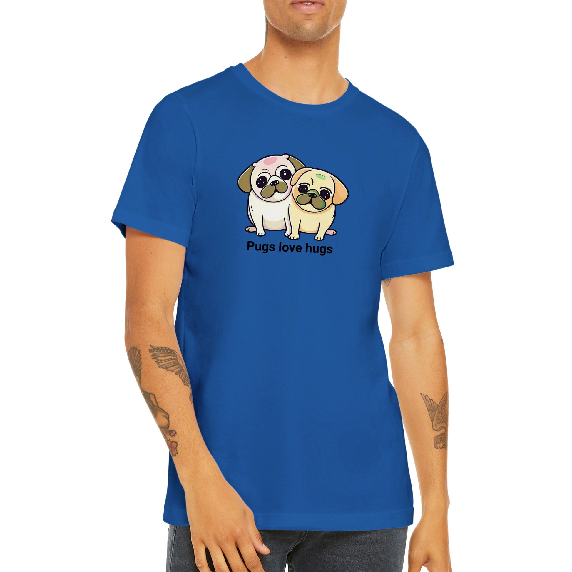 Torso of a young man with arm tattoos wearing a blue t-shirt with two pugs sitting snuggled next to each other. The pugs are drawn in a cartoon Kawaii-icon style and one is more white-beige and the other iis yellow-beige. Underneath the pugs are the words "pugs love hugs."