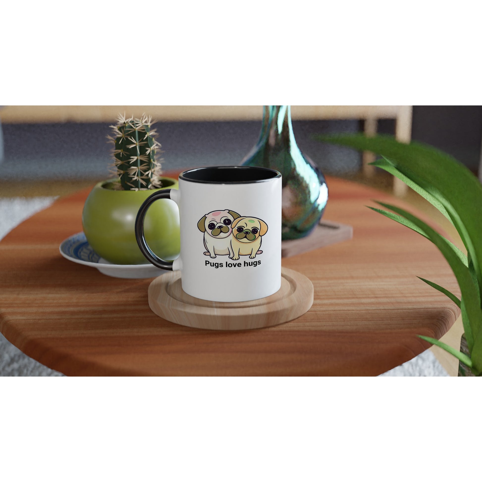 Round wooden end table with a potted cactus, a glass vase, and a ceramic mug on it. The mug is a white mug with black handle with two pugs sitting snuggled next to each other on it. The pugs are drawn in a cartoon Kawaii-icon style and one is more white-beige and the other iis yellow-beige. Underneath the pugs are the words "pugs love hugs."