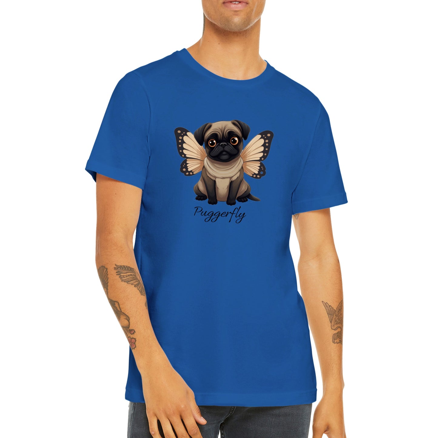 Torso of a young man with arm tattoos wearing a blue t-shirt with a cartoon style picture of a fawn-colored pug with orangey-beige butterfly wings attached to her back and big sad eyes. The word "Puggerfly" is beneath the image.