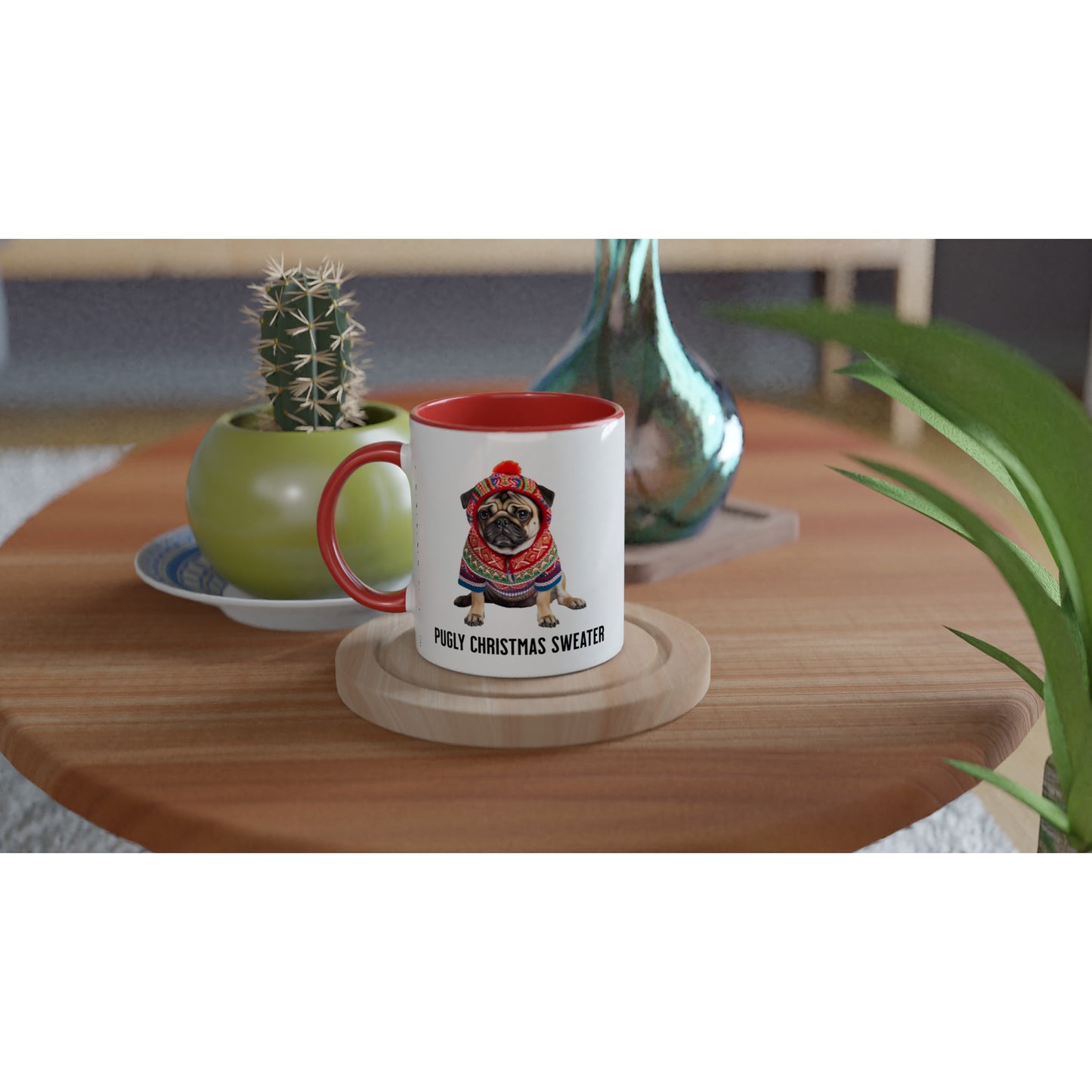 Round wooden end table with a glass vase, potted cactus, and white mug on it. The mug is a white ceramic mug with red handle, lip, and inside with a picture of a miserable-looking pug wearing an ugly Christmas sweater with a hood on it and the words "Pugly Christmas Sweater" below the image.