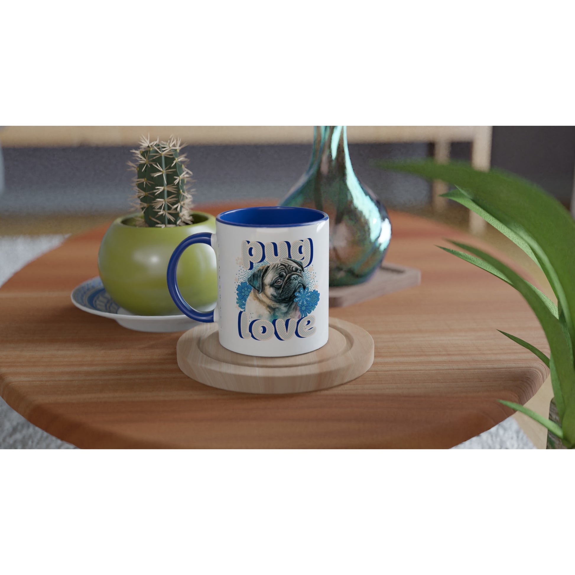 Round wooden end table with a potted cactus, glass vase, and mug on it. The mug is a white mug with a blue handle, rim, and inside with the design of a pug's head and shoulders surrounded by blue flowers and white stars and paw prints with the word "pug" above and the word "love" below in puffy bubble letters.