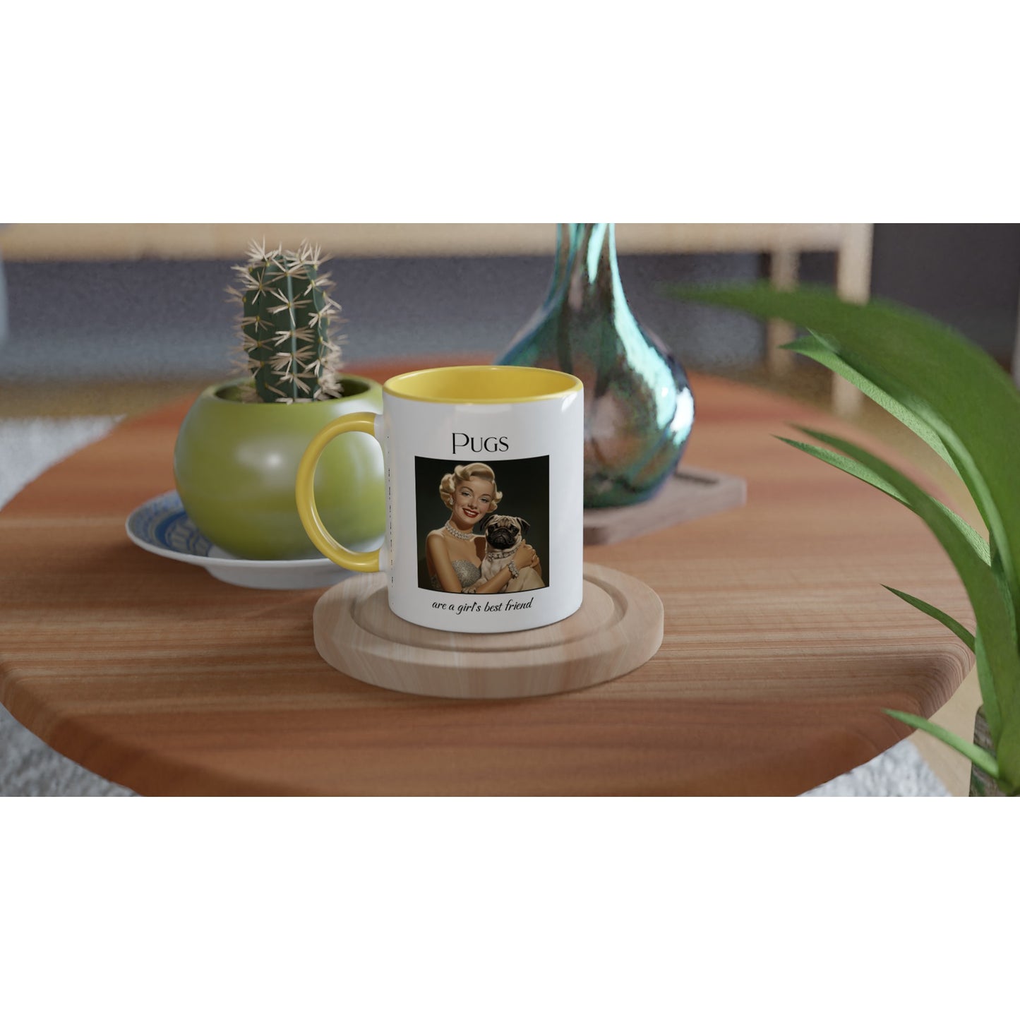 Round wooden coffee table with potted cactus, glass vase, and mug on it. It's a white mug with yellow handle, rim, and inside with Image of Marilyn Monroe wearing a chunky diamond necklace and bracelet and holding a fawn-colored pug who is wearing a matching diamond collar. The word "Pugs" is above the image and the words "are a girl's best friend" are under the image.