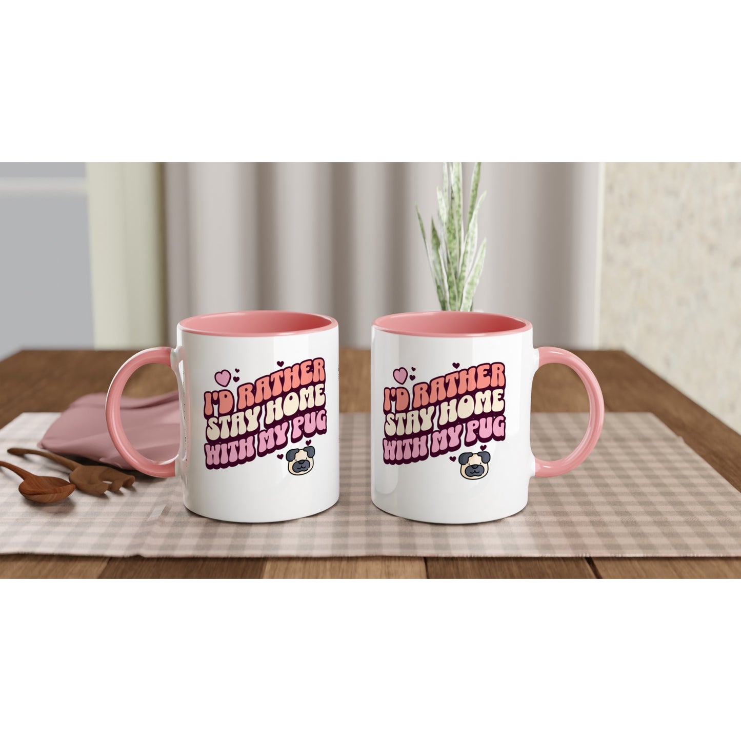 Two white mugs with pink handles and pink insides showing off the front and back of the mug with the words "I'd rather stay home with my pug" in an orangey-pink, beige, and pink colored bubble-style lettering on it and small hearts above the words to the left and a small heart above the words to the right with two other small hearts  and a picture of a cartoon pug face below the words on the right.