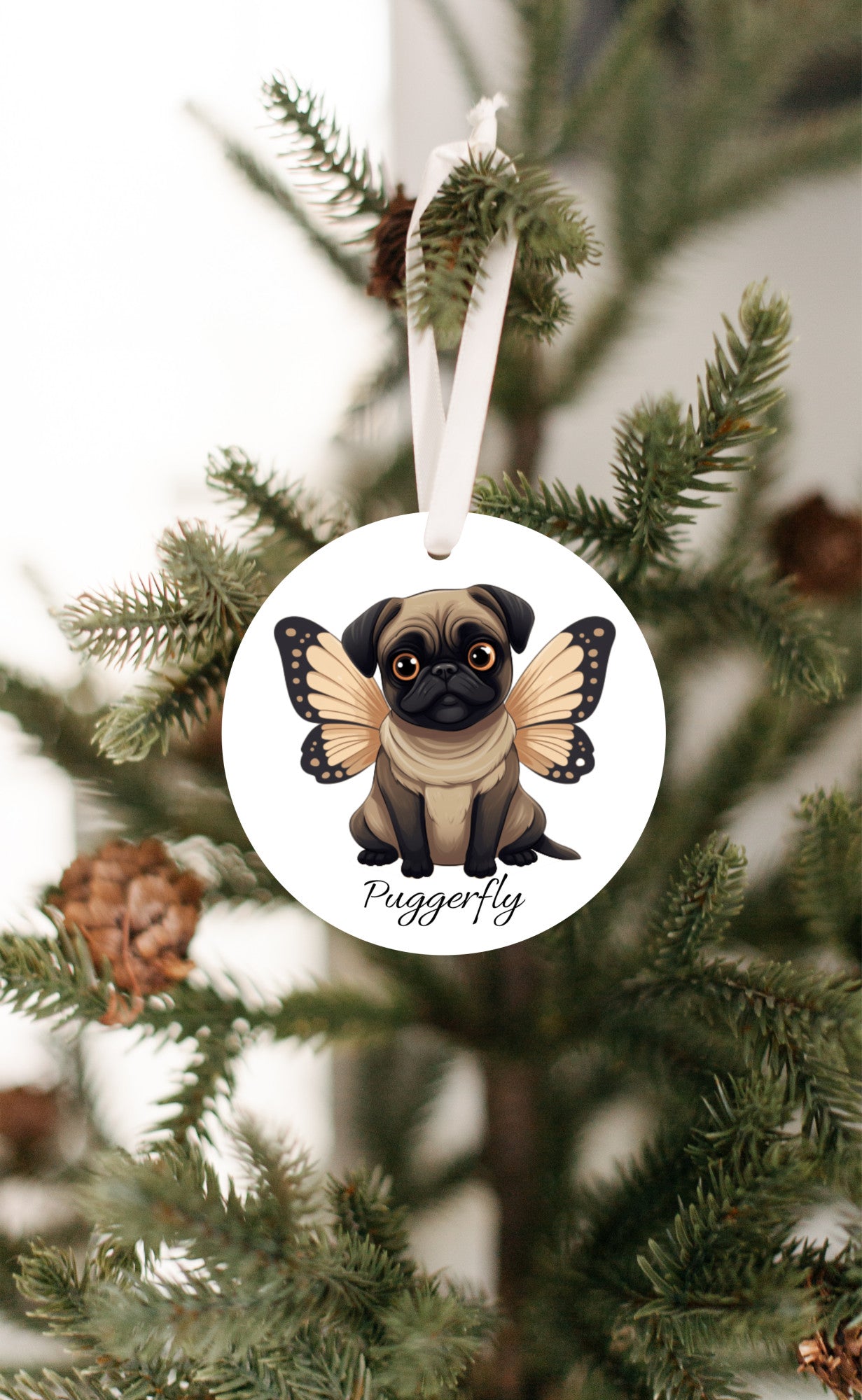 3 inch round white ornament hanging in a Christmas tree.  The ornament has a cartoon style picture of a fawn-colored pug with orangey-beige butterfly wings attached to her back and big sad eyes. The word "Puggerfly" is beneath the image.