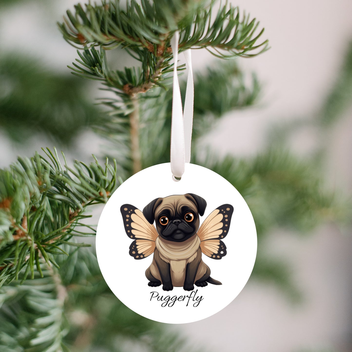 3 inch round white ornament hanging in a Christmas tree.  The ornament has a cartoon style picture of a fawn-colored pug with orangey-beige butterfly wings attached to her back and big sad eyes. The word "Puggerfly" is beneath the image.