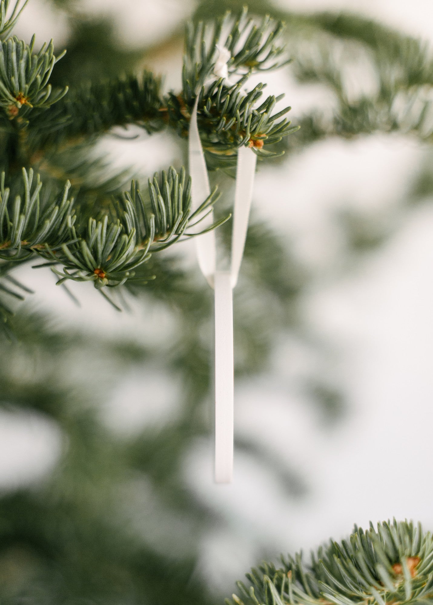 Side view of a 3 inch round white ornament hanging from a Christmas tree.