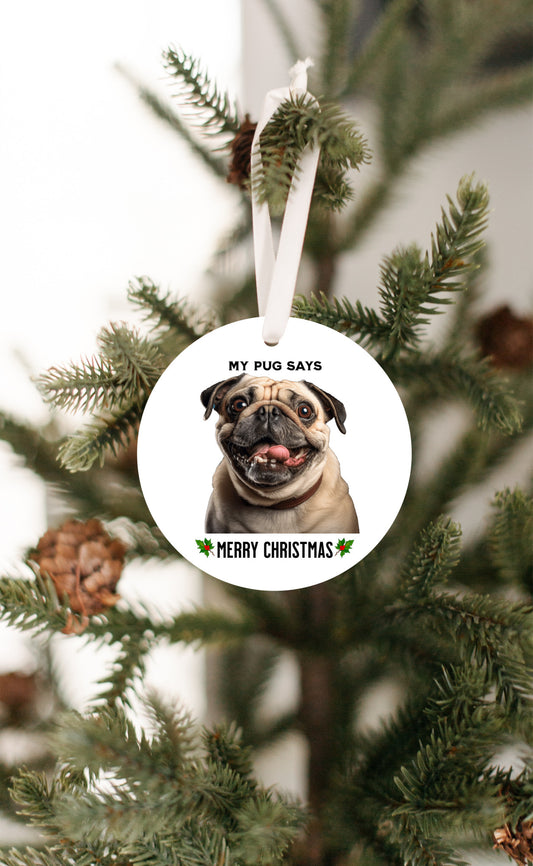 3 inch round flat white ornament hanging in a Christmas tree with a picture of the head and shoulders of a fawn-colored pug with the words "My pug says" above the pug and "Merry Christmas" below the pug. 