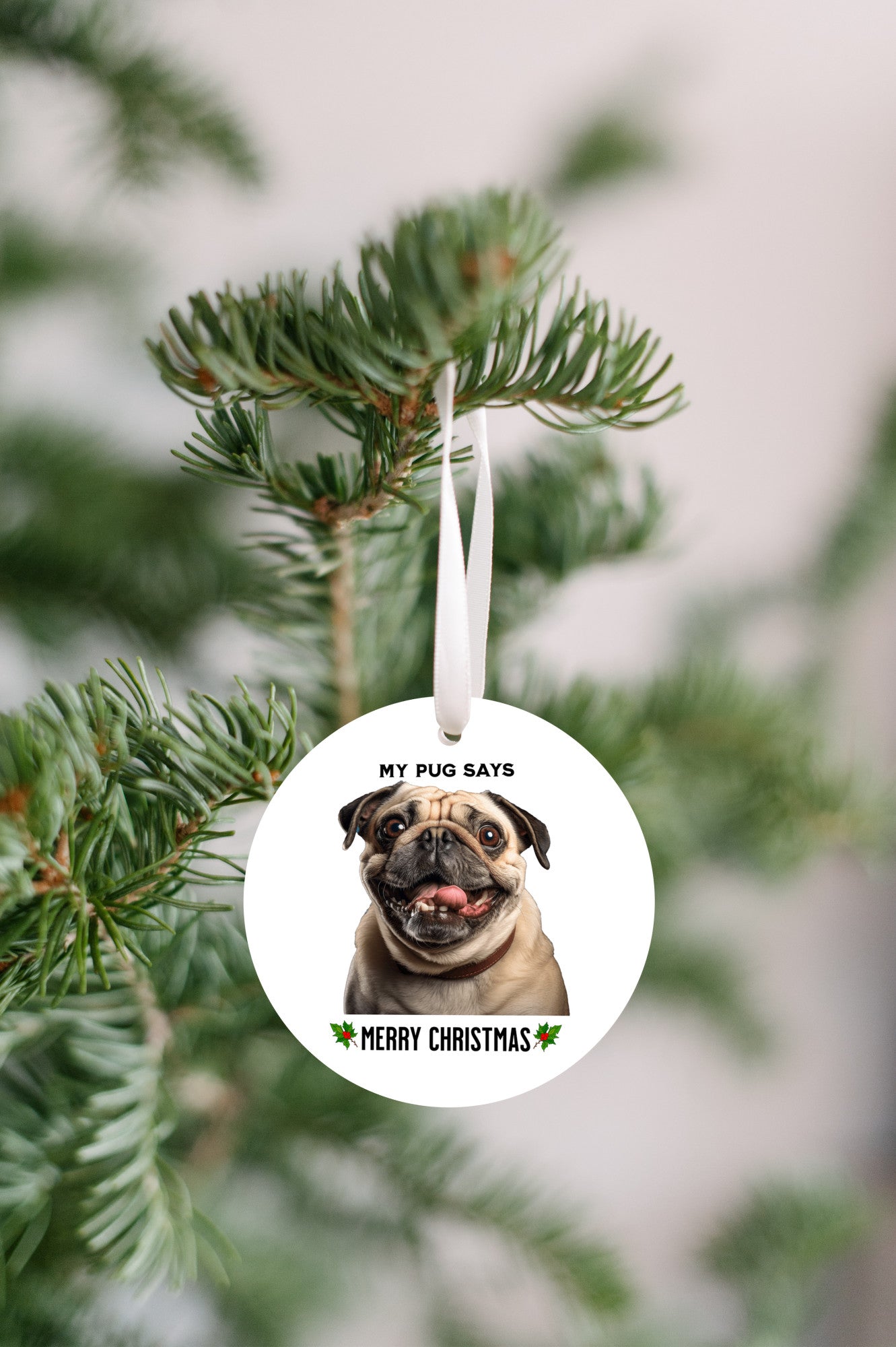 3 inch round flat white ornament hanging in a Christmas tree with a picture of the head and shoulders of a fawn-colored pug with the words "My pug says" above the pug and "Merry Christmas" below the pug. 