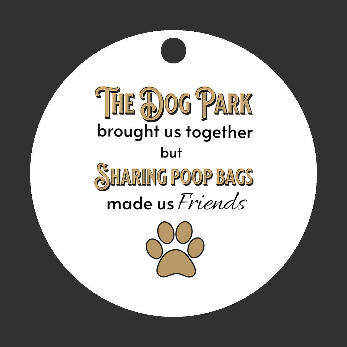 3 inch round flat white ornament on a black background. On the ornament are the words "The Dog Park brought us together but sharing poop bags made us friends" in black and gold letters. There is a gold pawprint beneath the words.